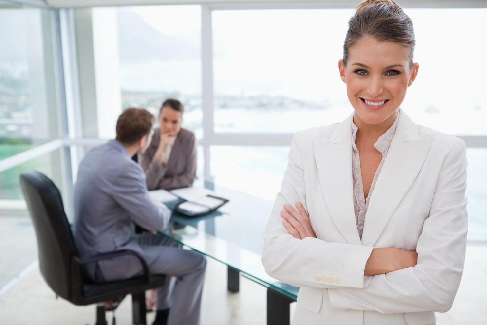 Smiling marketing manager standing in conference room with team sitting behind her